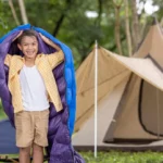 Junge beim Camping mit Schlafsack und Zelt