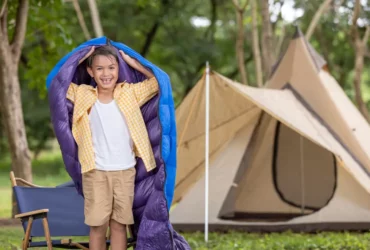 Junge beim Camping mit Schlafsack und Zelt