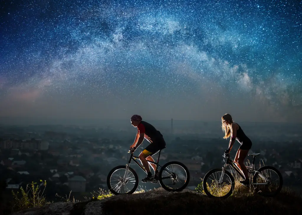 Sportliches Paar fährt nachts mit Beleuchtung Fahrrad unter Sternenhimmel